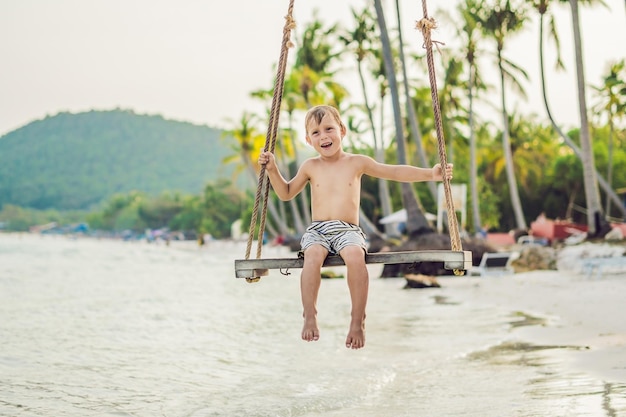 Niño feliz sentarse en columpio en la orilla del mar al atardecer