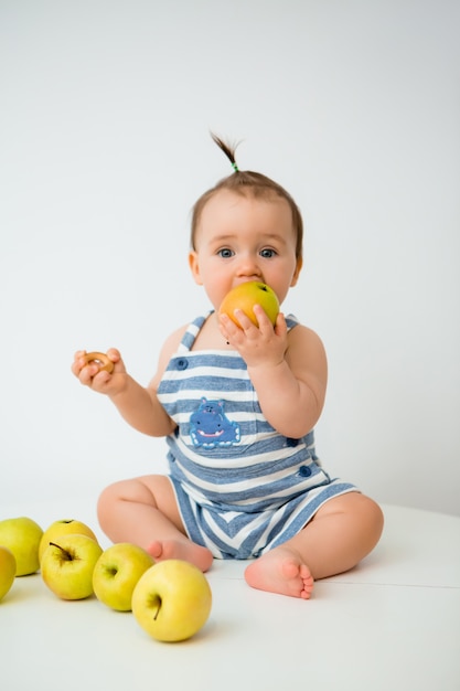 Niño feliz se sienta y come manzanas sobre un fondo blanco.