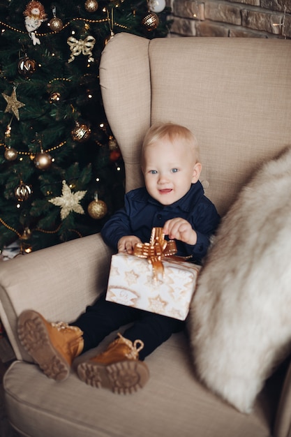 Niño feliz se sienta en el sillón en ambiente navideño y sonríe