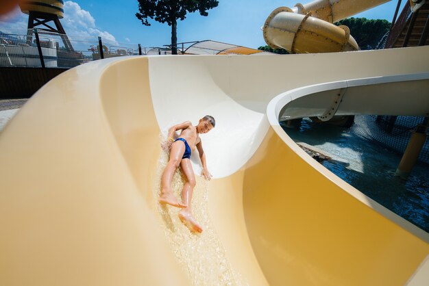 Un niño feliz de siete años desciende de los toboganes del parque acuático. Felices vacaciones vacaciones. Vacaciones de verano y turismo.