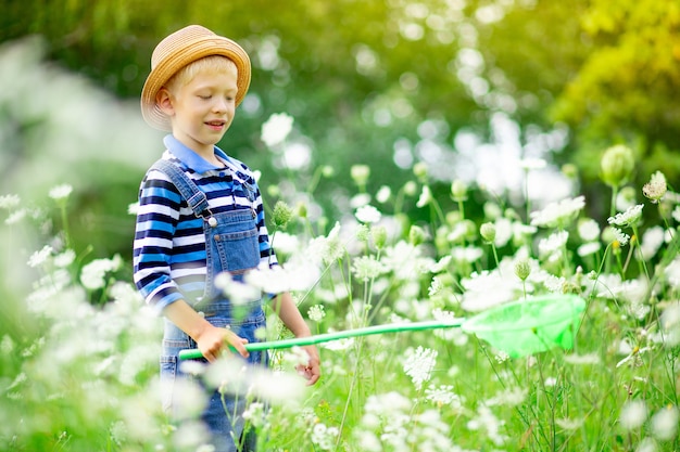 Niño feliz con sombrero camina por un campo con flores y atrapa mariposas con una red