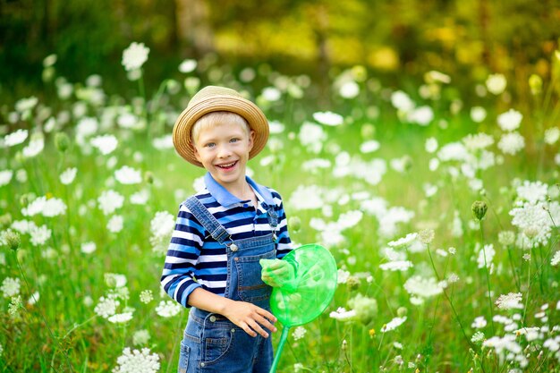 Niño feliz con sombrero camina por un campo con flores y atrapa mariposas con una red