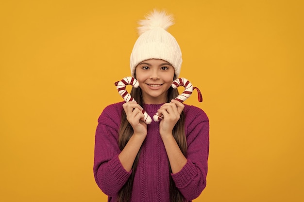 Niño feliz en sombrero de invierno niño con bastones de caramelo adolescente sobre fondo amarillo