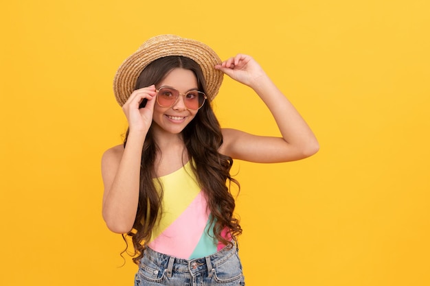 niño feliz con sombrero de paja de verano y gafas tiene el pelo rizado sobre fondo amarillo, diversión de verano.