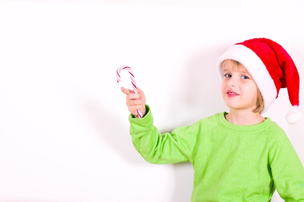 Niño feliz con sombrero rojo de Santa con dulces en la mano. Concepto de navidad.