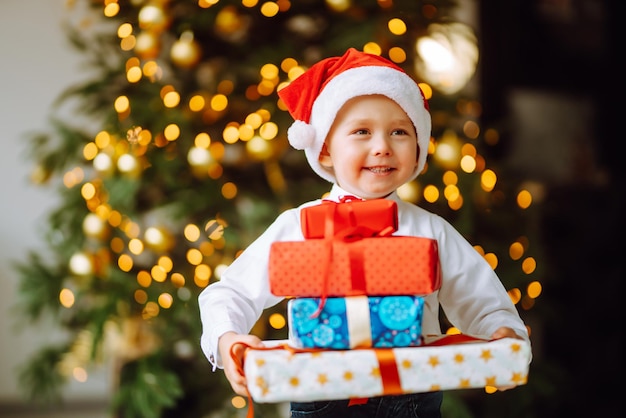 Niño feliz con sombrero rojo de Santa recibe regalos de Navidad. Niño divertido posando con regalos.