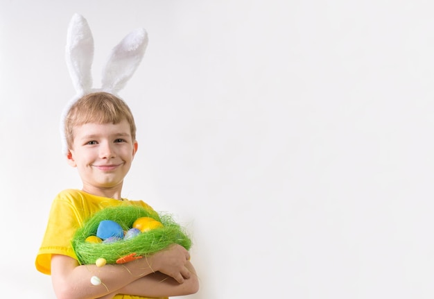 Niño feliz sonriendo en una camiseta amarilla en orejas de conejo y con coloridos huevos Concepto de Pascua con