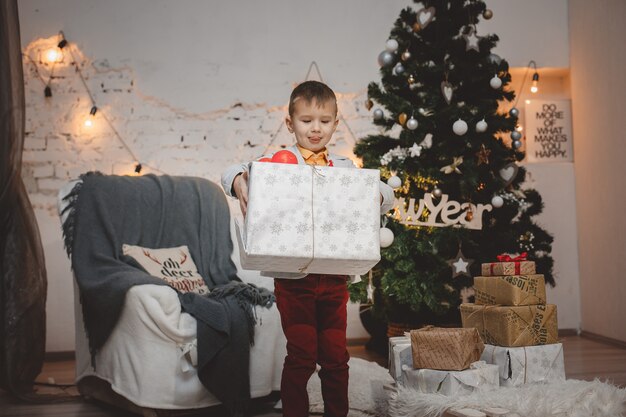 Niño feliz sonriente con caja de regalo cerca del árbol de Navidad
