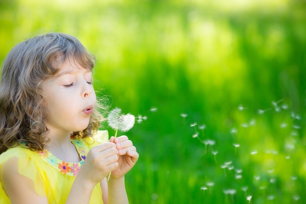 niño feliz soplando flor de diente de león al aire libre niña divirtiéndose en primavera sueño e imaginación