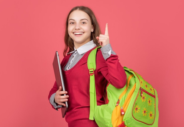 Niño feliz sostenga la computadora con mochila sobre fondo rojo inspirado con la idea
