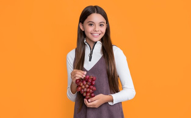 Niño feliz sostenga uvas saludables sobre fondo amarillo