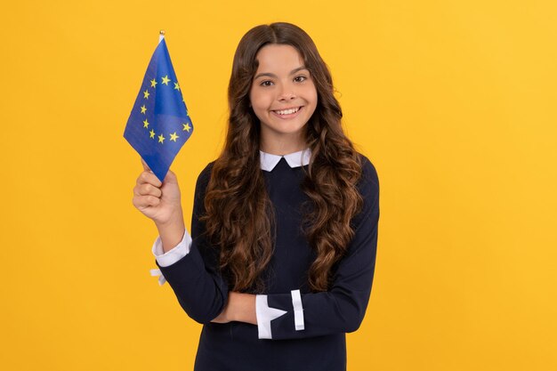 Niño feliz sosteniendo la bandera de la unión europea sobre fondo amarillo. visa de turista en el país schengen. niño niña viajar y estudiar en el extranjero. vacaciones en la eurozona. educación en la escuela de idiomas extranjeros.