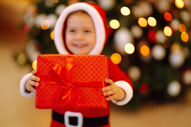 Niño feliz sosteniendo una caja de regalo roja en las luces de fondo