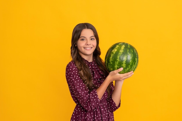 Niño feliz sosteniendo fruta fresca de melón de agua madura sobre fondo amarillo verano