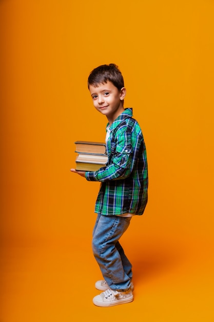 Niño feliz sosteniendo libros pesados aislado fondo amarillo. Concepto de educación