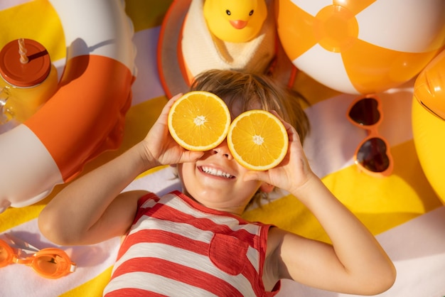 Niño feliz sosteniendo rodajas de fruta naranja como gafas de sol