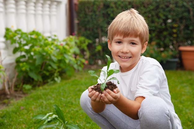 Niño feliz sosteniendo suelo con planta verde en sus manos