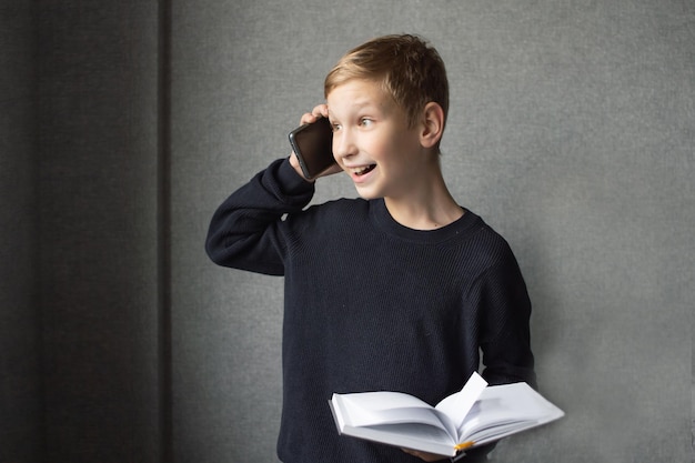 Un niño feliz sostiene un libro en sus manos y habla por teléfono