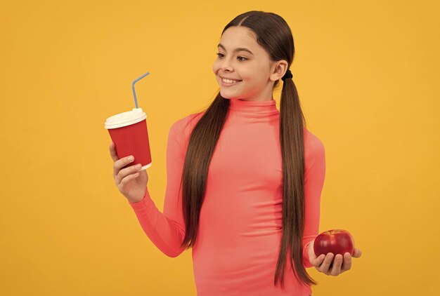 Niño feliz con taza de café para llevar y manzana sobre fondo amarillo a la hora del almuerzo