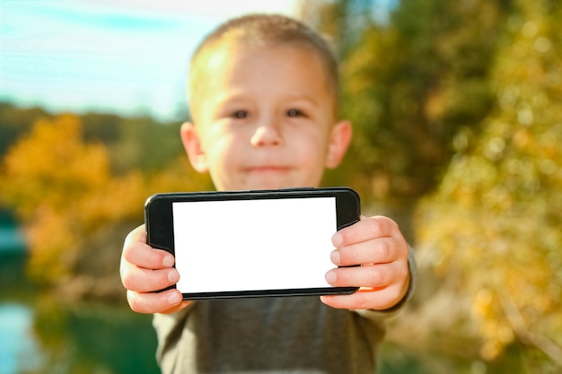 Un niño feliz con teléfono tomando selfie en la naturaleza en el viaje del parque