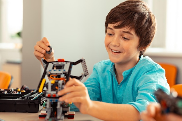 Foto niño feliz terminando su trabajo en el complicado robot hecho con juego de construcción durante la lección de ciencias