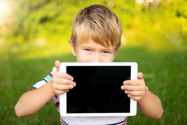 Foto niño feliz tiene una tableta al aire libre en un parque de verano