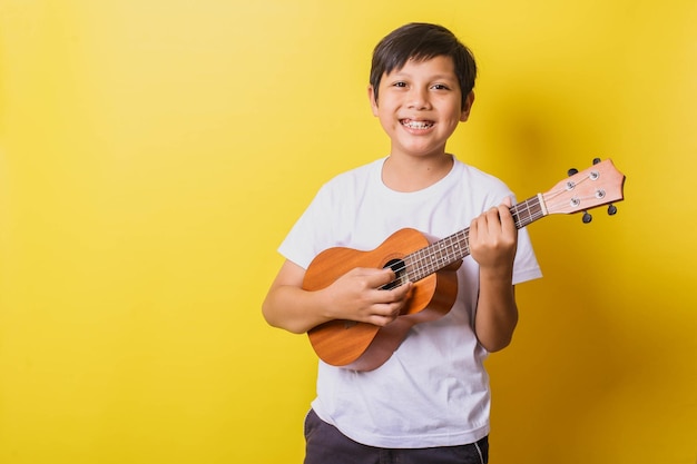 Niño feliz tocando el ukelele aislado sobre fondo amarillo