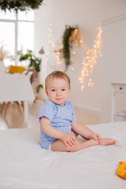 Niño feliz en traje azul se sienta en su casa en la cama jugando con juguetes en desarrollo