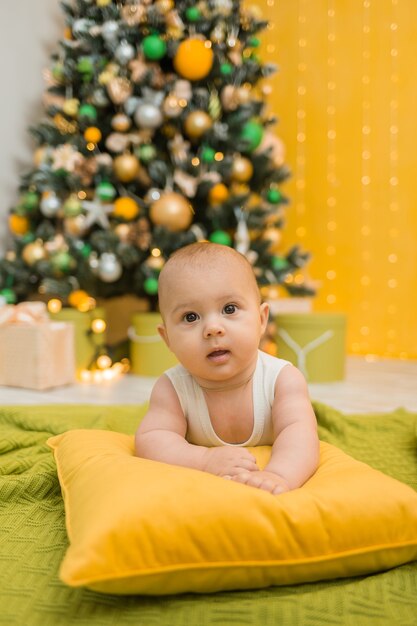 Niño feliz en un traje blanco yace sobre una almohada con el telón de fondo de un árbol de Navidad. Orientación vertical