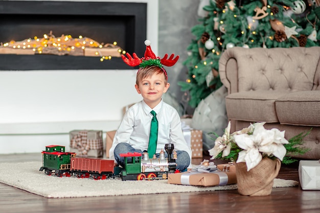 Niño feliz con un tren de juguete de regalo bajo el árbol de Navidad en una mañana de Año Nuevo