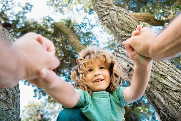 Niño feliz trepando a un árbol durante el verano la mano del padre