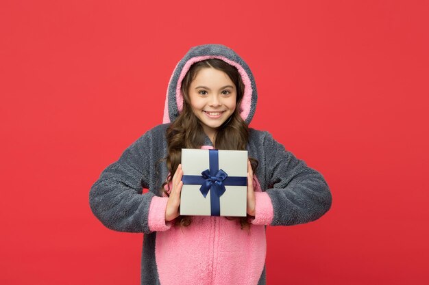 Un niño feliz usa pijamas de animales kigurumi y sostiene una caja de regalo feliz cumpleaños