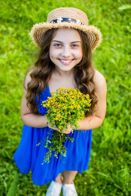 Un niño feliz usa un sombrero para el sol con el pelo largo y un vestido de verano de moda con un regalo de flores