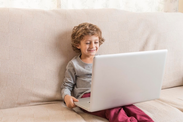 Un niño feliz usando una computadora portátil en el sofá.