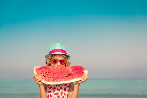 Niño feliz en vacaciones de verano Niño comiendo sandía en la playa Concepto de comida sana