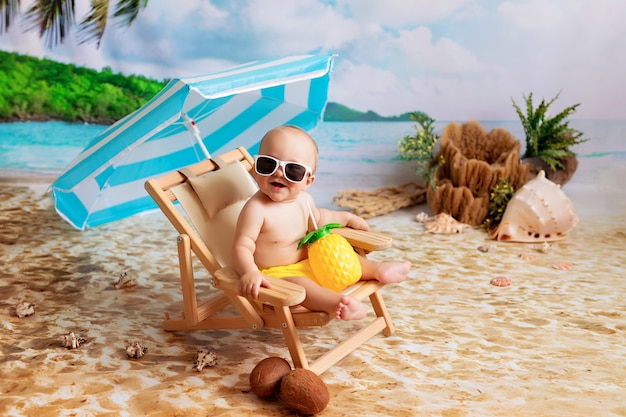 Niño feliz en vasos se encuentra en una tumbona, toma el sol en una playa de arena junto al mar y bebe jugo