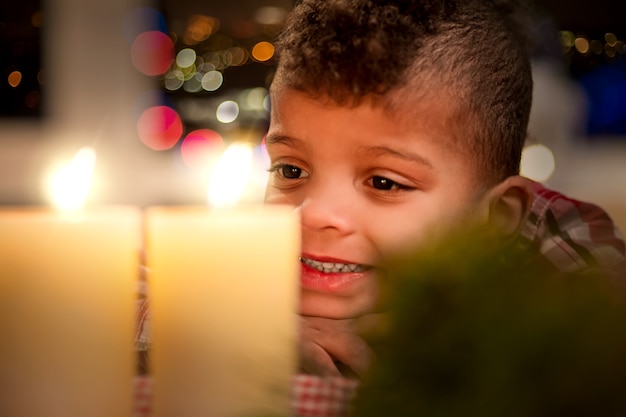 Niño feliz y velas navideñas. Niño mira felizmente velas. Las vacaciones siempre son divertidas. No puedo esperar a ver regalos.