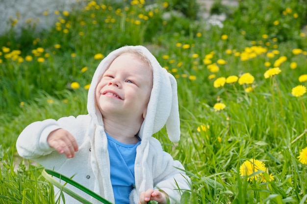 Niño feliz vestido como conejo se sienta en un campo con dientes de león