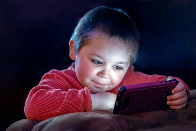 Un niño feliz viendo dibujos animados en el teléfono celular de su madre.