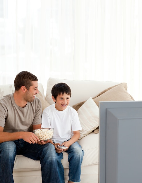 Niño feliz viendo la televisión con su padre en el sofá