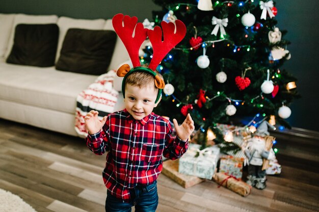Niño feliz se viste en la cabeza de las astas de un ciervo cerca del árbol de Navidad. Familia en la noche de Navidad. Disfrutando de unas vacaciones en familia. Feliz navidad y próspero año nuevo.