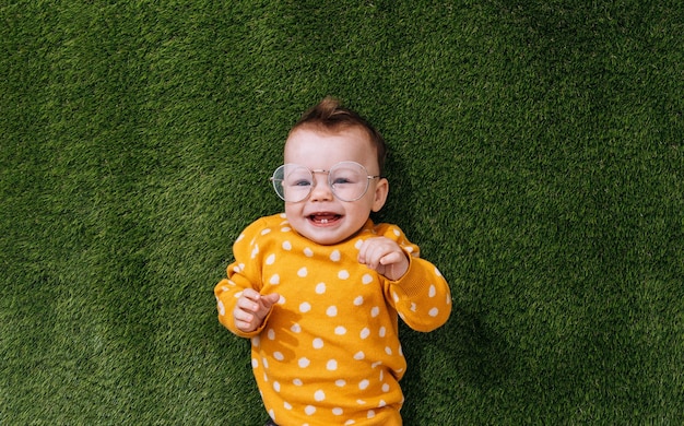 Un niño feliz yace sobre la hierba verde con un suéter amarillo y gafas