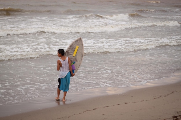 Niño filipino con tabla de surf en la playa