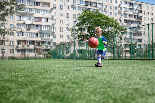 Niño en forma azul y verde jugando al fútbol en campo abierto en el patio de un joven jugador de fútbol