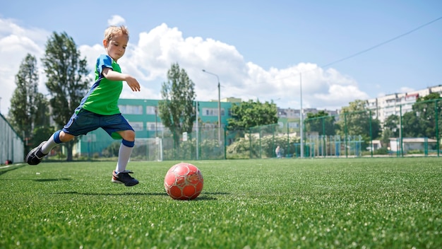 Niño en forma azul y verde jugando al fútbol en campo abierto en el patio de un joven jugador de fútbol