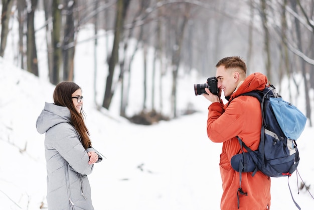 Niño de fotografía rubia haciendo fotos de su novia en el fondo de paisajes de invierno mientras camina en el bosque