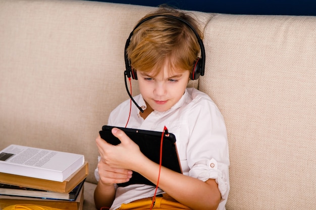 Un niño con gafas y auriculares está aprendiendo lecciones con una tableta y libros.