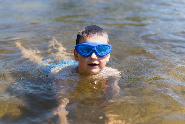 Un niño con gafas azules nada en el lago.