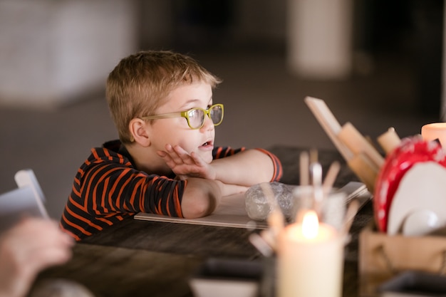 Niño con gafas grandes esculpe de arcilla con interés