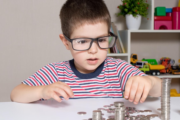 Un niño con gafas, un joven empresario juega con monedas y ahorra dinero.